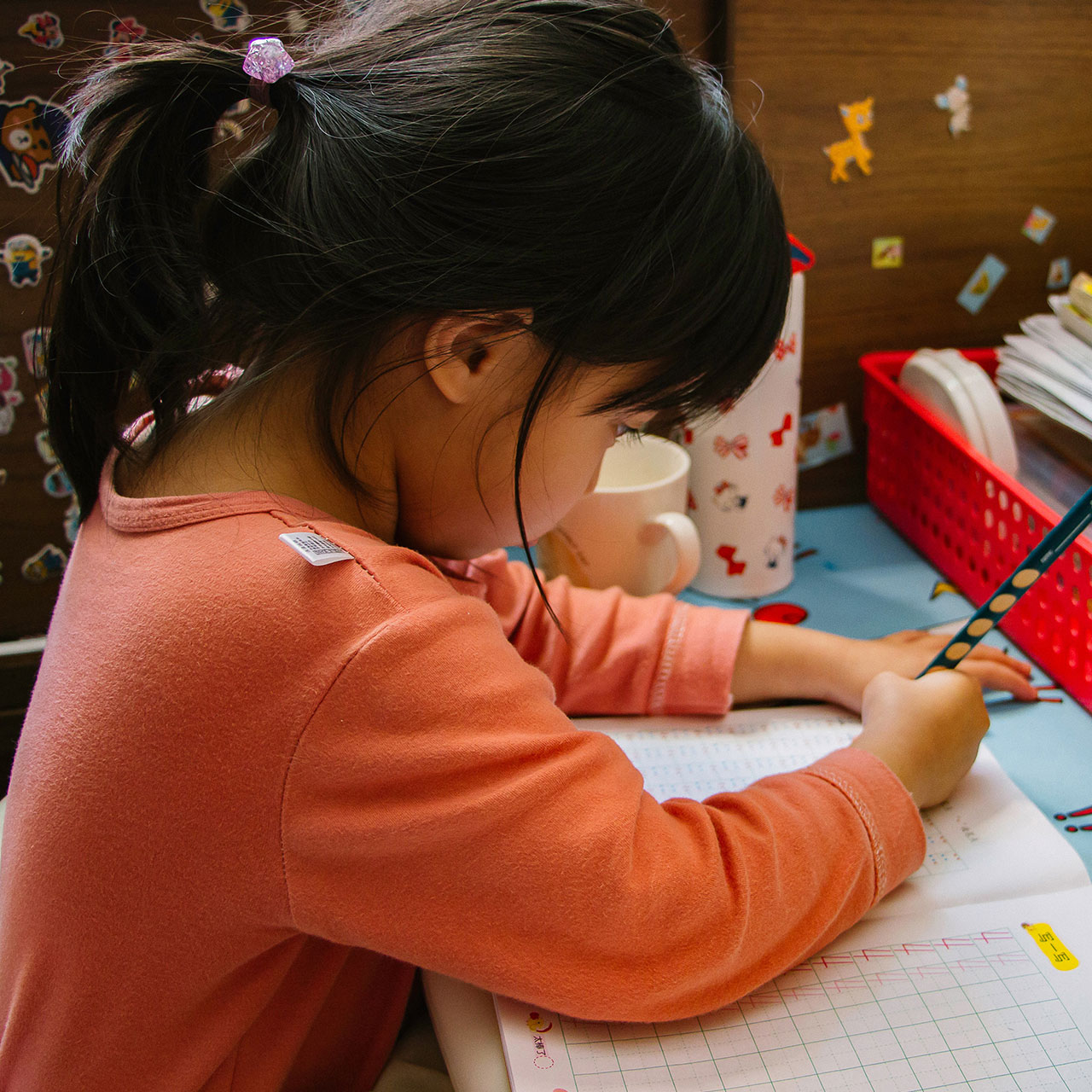 Une enfant est assise à sa table de classe en train de travailler sur son cahier.